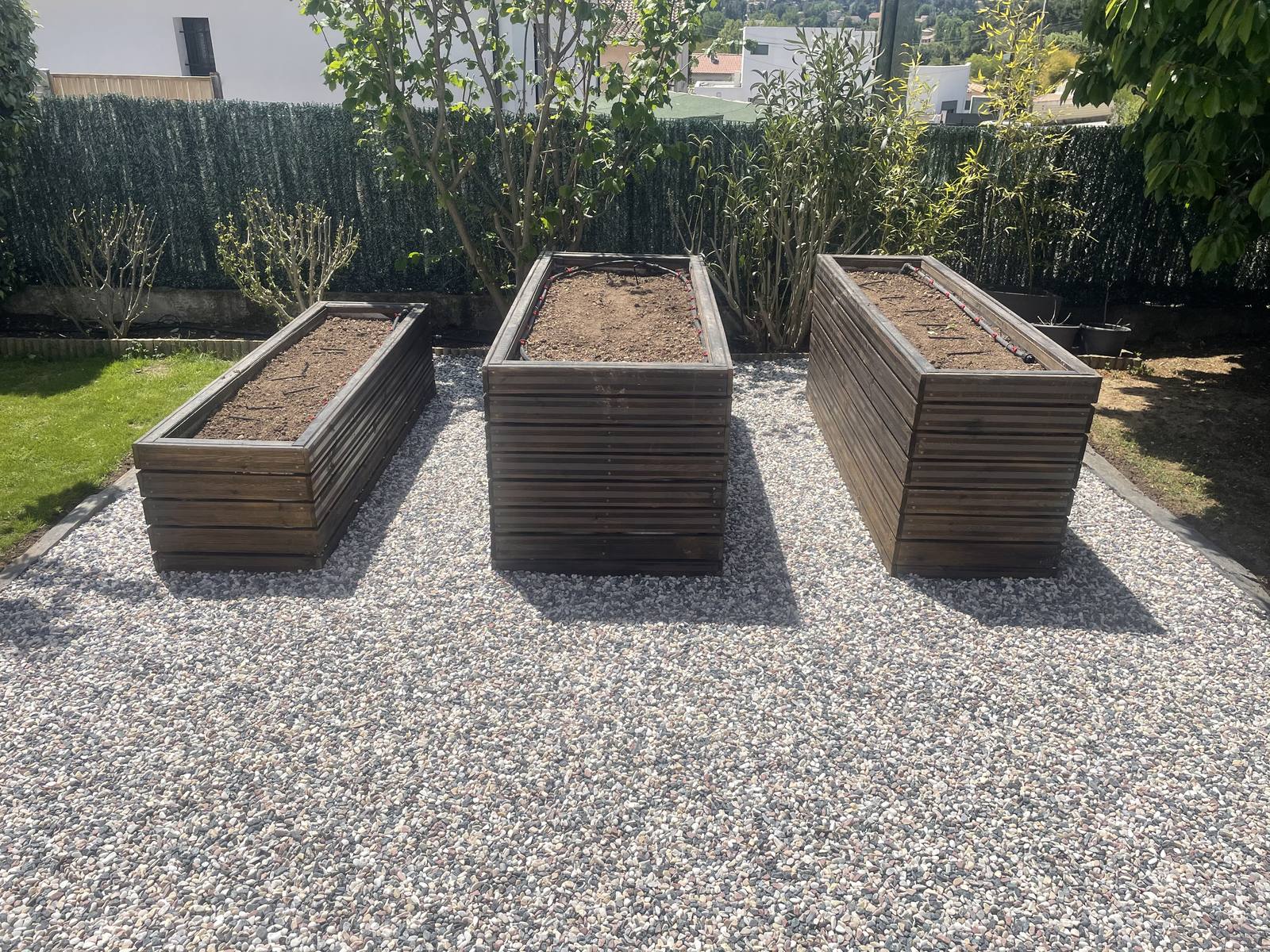 Trois bacs potagers en bois installés sur un lit de gravier